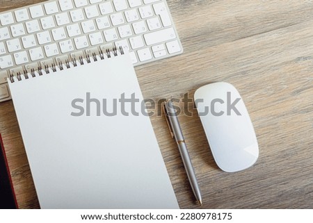 Notepad with pen and keyboard on wooden table