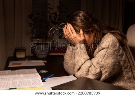Tired exhausted student trying to study in the night at home scratching her eyes with her hands and holding her glasses. Young woman falling asleep while studing at night in her room Royalty-Free Stock Photo #2280983939