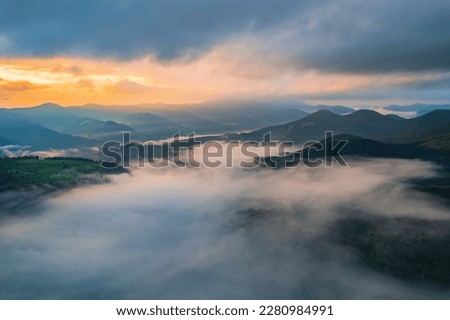 Mountains in clouds at sunrise in summer. Aerial view of mountain peak with green trees in fog. Beautiful landscape with high rocks, forest, sky. Top view from drone of mountain valley in low clouds Royalty-Free Stock Photo #2280984991