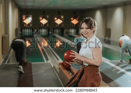 Shot of a cute girl holding bowling ball and looking at camera while preparing to throwing in the bowling club.