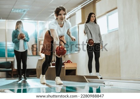 A cute girl throwing the bowling ball while her friends are standing in the back.