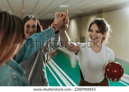Three young woman giving high five while preparing to throwing at the bowling club.