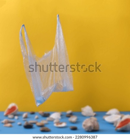 In focus is a plastic bag with a plastic bottle on a blurred background of shells on a blue sea background with a sunny yellow at the top. Selective focus. Ecotrend concept: no plastic, save the ocean