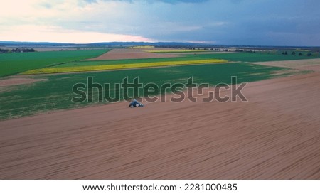 AERIAL: Tractor planting seeds in the field for autumn harvest on a cloudy day. Farm worker sowing crops with agricultural working machinery. Land usage for ecological and organic vegetable production