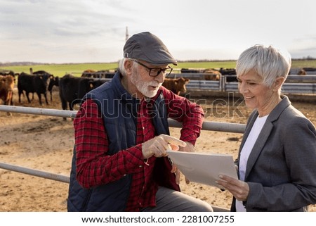 Mature farmer talking with finance consultant woman at cattle farm about loan and business