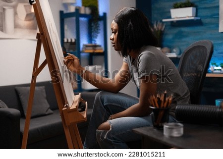 Artistic woman creating pencil sketch on easel at art workplace. African american female artist making hand drawing on canvas, sitting at home made sketching atelier in bedroom. Royalty-Free Stock Photo #2281015211