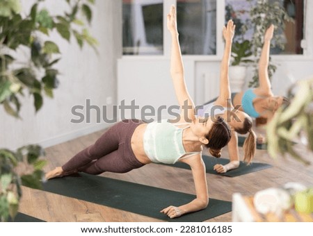 Concentrated young woman practicing power yoga during group training in fitness studio, standing in balancing side plank pose Vasisthasana Royalty-Free Stock Photo #2281016185