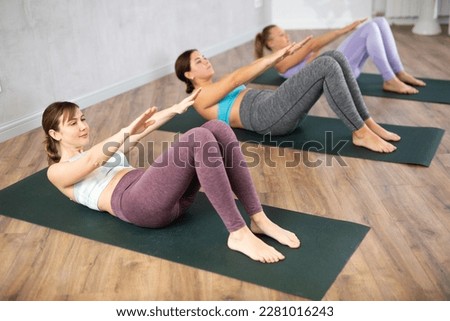 Young sporty woman doing abdominal crunches with outstretched arms to strengthen abs and core muscles during group yoga class in fitness studio Royalty-Free Stock Photo #2281016243