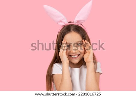 Pretty nice girl smiling and looking at the camera tries to cover her face with palms wearing bunny ears on head, Easter concept.