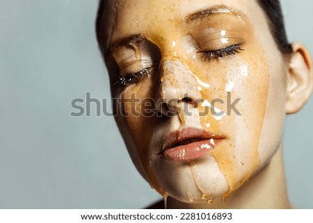 Closeup portrait of attractive calm young woman with freckles and honey on face, keeps eyes closed, having serious expression. Indoor studio shot isolated on gray background.