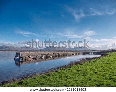 Mullaghmore pier and beautiful nature scenery in the background. Warm sunny day with blue cloudy sky. Popular travel area. Ireland. Atlantic ocean. Fish boats and yachts.