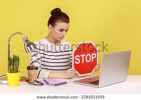 Woman manager wearing striped shirt showing stop red sign to laptop screen, avoiding conflicts, afraid of workplace bullying. Indoor studio studio shot isolated on yellow background. Royalty-Free Stock Photo #2281021039