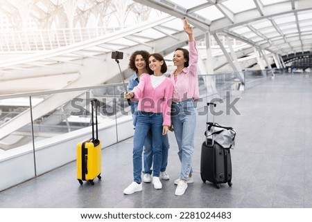 Three Cheerful Female Friends Taking Photo With Selfie Stick At Airport, Group Of Happy Young Women Travelling Together, Posing At Smartphone Camera While Standing With Luggage At Terminal Hall