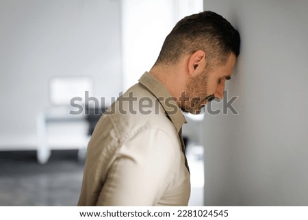 Upset middle aged businessman banging his head against wall in despair looking stressed, having problems at work. Business failure, unsuccessful negotiations, failed job interview concept Royalty-Free Stock Photo #2281024545