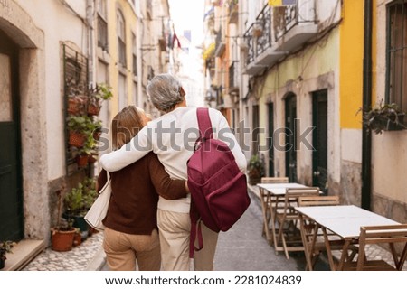 Vacation Tour Offer. Back View Of Senior Couple Hugging And Carrying Backpack Walking On Lisbon Street, Enjoying Sightseeing Outdoors. Travel And Tourism In Europe Concept Royalty-Free Stock Photo #2281024839