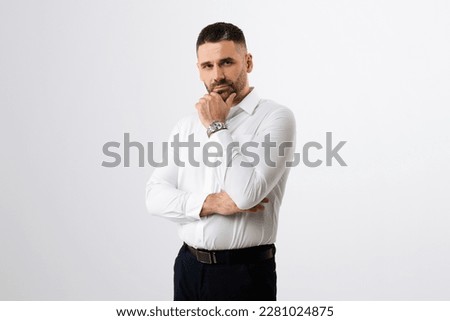 Pensive businessman touching chin and looking at camera, male entrepreneur thinking about business offer or new startup while standing on grey background