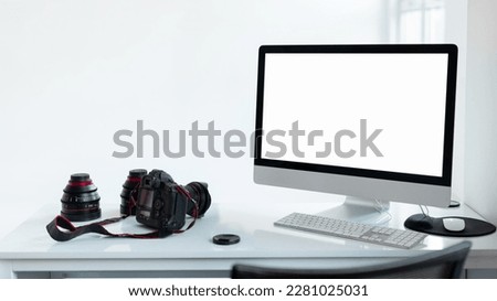 Photographer workplace with blank screen computer monitor and camera accessories, white studio background, mockup template for your design