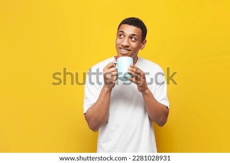 young african american guy in white t-shirt holds cup of coffee on yellow isolated background, man with drink looks at copy space Royalty-Free Stock Photo #2281028931