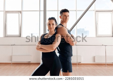beautiful athletic couple in sportswear stands in the gym in morning, fitness girl and coach man stand back to back in training in bright room Royalty-Free Stock Photo #2281031011