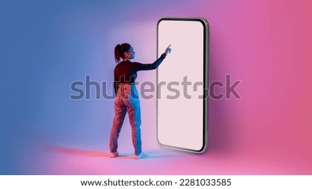 African american lady touching screen of giant smartphone in neon light, mockup for mobile app or website design. Black woman interacting with big cellphone, space for ad Royalty-Free Stock Photo #2281033585
