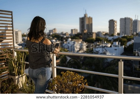Young Latin woman taking picture of the balcony view of the city with her mobile phone
