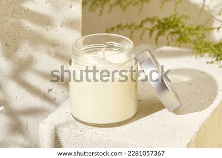 Aesthetic composition with aromatic candle in jar on concrete podium. Mockup soy wax candle in natural style. Scented handmade candle with green leaves.  Handmade spa product  from soy wax in glass Royalty-Free Stock Photo #2281057367