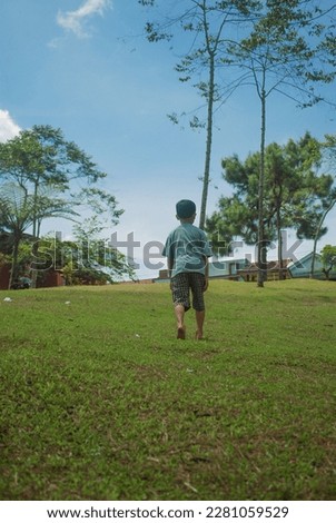 A child in a green T-shirt was climbing a hill, against a backdrop of pine trees and a clear sky