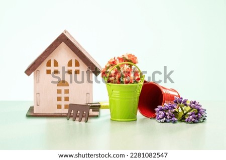  Gardening concept. Gardening tools, flowers in small metal bucket and model of house.