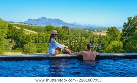 couple of men and women in a swimming pool looking out over the Vineyards and mountains of Stellenbosch South Africa. Royalty-Free Stock Photo #2281089953