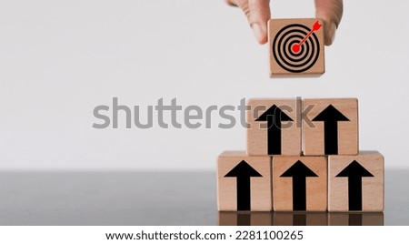 Goal Achievement and Purposefulness,challenge in busiess concept.,Hand  arranges a wooden block with dartboard icon stack in pyramid shape over white background with copyspace. Royalty-Free Stock Photo #2281100265
