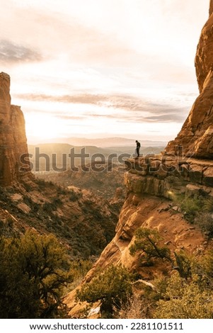 Young man stands looking down dramatic cliff at sunset at Cathedral Rock Sedona Royalty-Free Stock Photo #2281101511