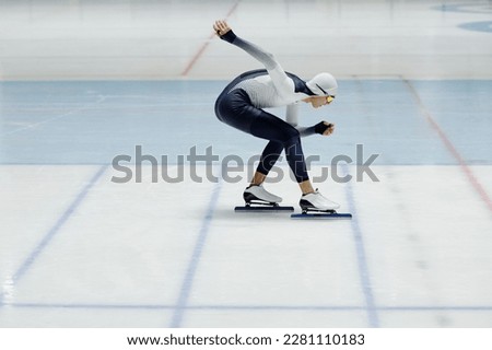 Side view of young athlete in sports uniform bending forwards while sliding on ice rink and practicing new movements on arena