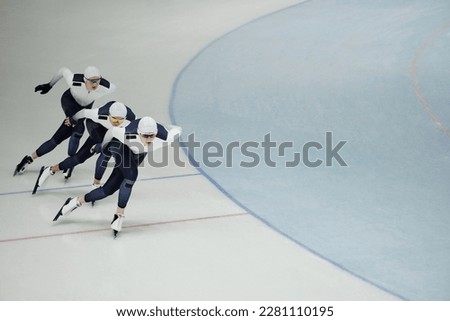 Row of three young active athletes on skates sliding along ice rink while practicing some exercises during training before competition