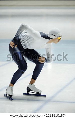 Active young man in speed skating uniform bending and sliding forwards on ice rink while preparing for short track competition on arena