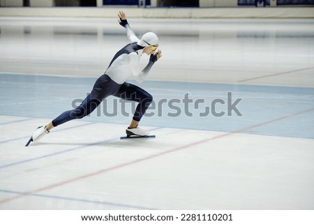 Side view of young active man in sports uniform and eyeglasses having short track speed skating training while sliding on ice inside arena