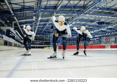 Young male ice skater in sports uniform and two more sportsmen behind him sliding forwards along rink while taking part in competition