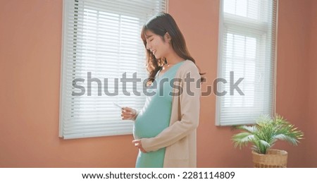 asian pregnant woman standing by the window happily looking at ultrasound photo enjoy her motherhood moment