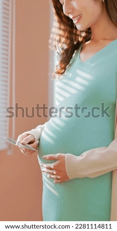 Closeup of Asian pregnant woman standing by the window happily looking at ultrasound photo enjoying her motherhood moment