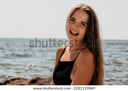 Woman summer travel sea. Happy tourist in hat enjoy taking picture outdoors for memories. Woman traveler posing on the beach at sea surrounded by volcanic mountains, sharing travel adventure journey