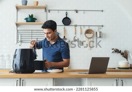 Happy handsome man cooking healthy food with recipe by Air Fryer machine and using laptop computer in the modern kitchen at home on sunny day. Watching or Learning with Technology connection. Royalty-Free Stock Photo #2281125855