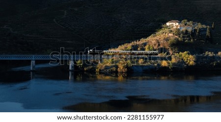 Tourist train in the douro valley, passing on the iron bridge and illuminated by the rays of the early morning sun - Port wine vineyards in the background mountains - Pocinho, Portugal