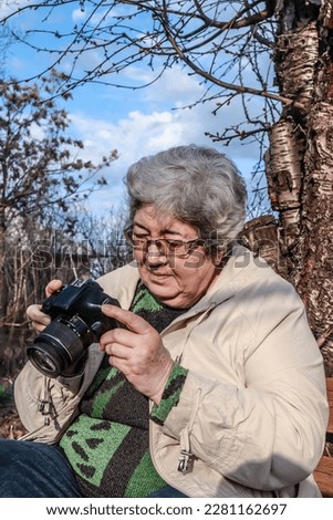 an elderly gray-haired woman professionally photographs nature.Grandmother - stock photographer