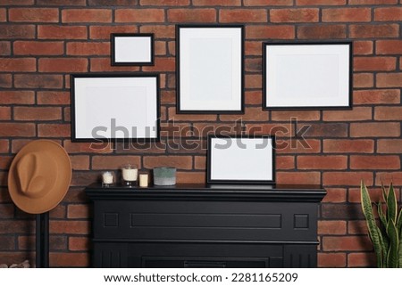 Empty frames, hat and scented candles on fireplace indoors