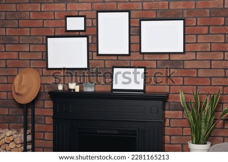 Empty frames hanging on brick wall, fireplace and potted plant candles indoors