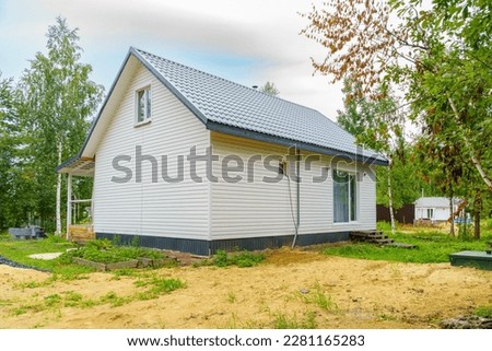 Simple two-story white country house with gable roof on plot in village Royalty-Free Stock Photo #2281165283