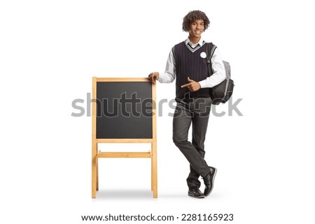 Full length portrait of a male african american student in a uniform leaning on blackboard isolated on white background