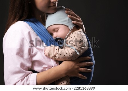 Mother holding her child in sling (baby carrier) on black background, closeup