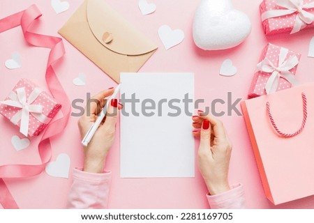 top view photo of valentine day decor female hands holding letter with envelope, small gift box and heart decoration on isolated pastel colored background with empty space.