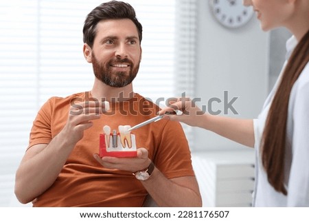 Doctor with educational model of dental implant consulting patient in clinic Royalty-Free Stock Photo #2281176507