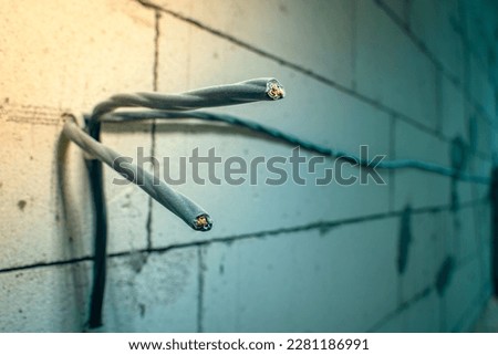Close-up of two three-wire wires attached to the wall. Wiring of electrical wiring on the wall of aerated concrete bricks. Power electrical wires in black braid for sockets Royalty-Free Stock Photo #2281186991
